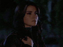 a woman wearing a black leather jacket and a gold necklace looks at the camera