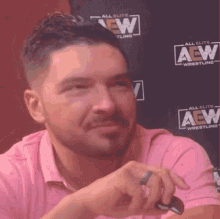 a man in a pink shirt is sitting in front of a wall that says aew wrestling