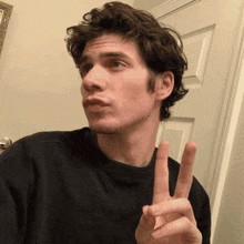 a man in a black shirt is making a peace sign with his fingers