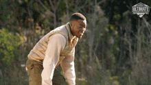 a man in a vest is standing in the woods with the word ultimate on the bottom left