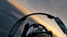 a person in a cockpit of a plane with a sunset behind them