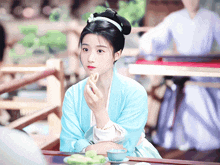 a woman in a blue dress is sitting at a table with a cup of tea in front of her