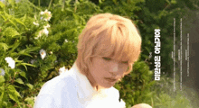 a young boy with blonde hair is standing in front of a bush with flowers and a sign that says ' a ' on it