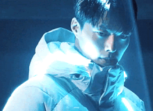 a man wearing a white jacket with a hood looks at the camera in a dark room