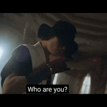 a man in a white vest and black hat is asking who are you