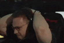 a man wearing headphones and glasses is sitting in a chair with his hands behind his head .