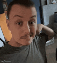 a man with a mustache is making a funny face while wearing a grey shirt .
