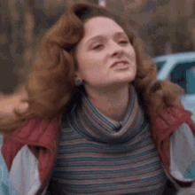 a woman with red hair is making a funny face while wearing a striped shirt and a jacket .