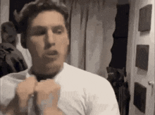 a man in a white shirt is adjusting his tie in front of a door .
