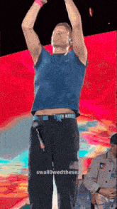 a man in a blue shirt and black pants is standing on a stage with his hands in the air .