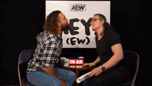 two men kissing in front of a sign that says aew wrestling