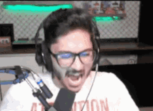 a man wearing headphones and a shirt that says attention is screaming into a microphone .