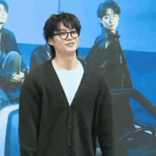 a young man wearing glasses and a black cardigan is standing in front of a group of people