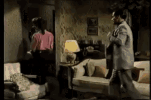 a man and woman are standing in a living room with a couch and a lamp .