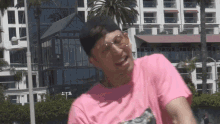 a man wearing a pink t-shirt and sunglasses is standing in front of a building