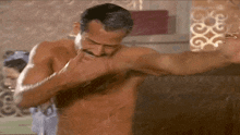 a shirtless man with a mustache is taking a shower with his arms outstretched .