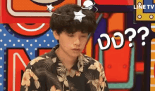 a young man with a star on his head is sitting in front of a colorful background with a question mark .