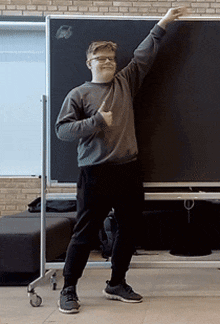 a young man stands in front of a blackboard with his arm in the air
