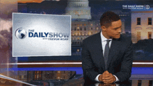 a man in a suit and tie is sitting in front of a screen that says the dailyshow with trevor noah