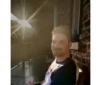 a man is sitting on a porch with the sun shining through the blinds
