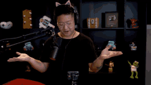 a man wearing headphones and glasses stands in front of a microphone with his arms outstretched