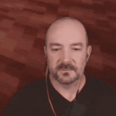 a bald man with a beard wearing earbuds and a ring on his finger