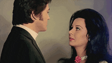 a man and a woman are looking at each other and the woman is wearing a pearl necklace