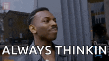 a man is standing in front of a window with the words `` always thinkin '' on his face .