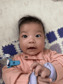 a baby laying on a blanket with a blue pacifier clip around his neck