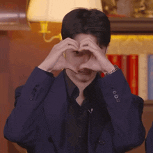 a man in a suit and black shirt is making a heart shape with his hands