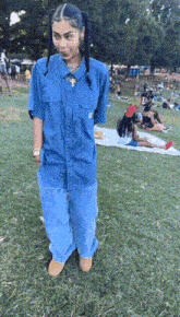 a woman in a blue shirt and blue pants is standing in a park .