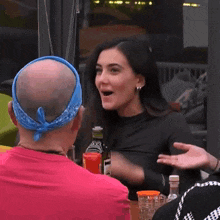 a bald man wearing a blue bandana is talking to a woman while sitting at a table .