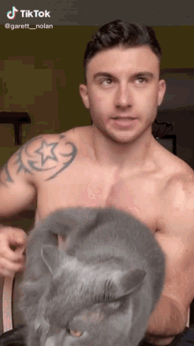 a shirtless man holds a gray cat in his arms with a tiktok watermark on the bottom