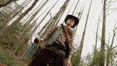a man in a cowboy hat and scarf is holding a gun in the woods