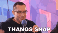 a man with glasses is talking into a microphone with the words thanos snap below him