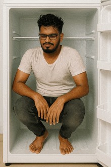 a man with glasses sits in an empty refrigerator