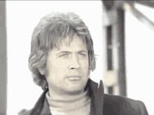 a man wearing a turtleneck and a black jacket looks to his left