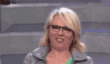 a woman wearing glasses and a gray jacket is making a face .