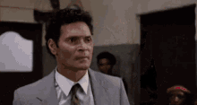 a man in a suit and tie is standing in a room with a group of people .