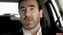 a man with a beard is sitting in the back seat of a car and making a funny face .