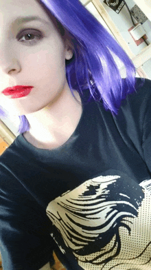 a woman with purple hair is wearing a black shirt with a picture of a woman 's face on it