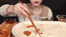a woman is using chopsticks to eat a bowl of food