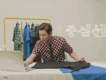 a man in a shirt and tie is folding a shirt in front of a laptop that says xhan on the bottom