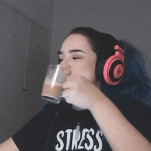 a woman wearing headphones and a shirt that says stress drinks from a glass