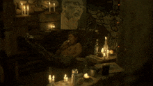 a man sits in a dark room with candles and a picture on the wall
