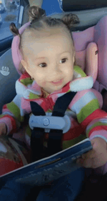 a little girl in a car seat holds a book that says " i love you " on it