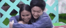 a man and a woman are hugging each other and smiling in front of a blue fence .