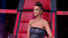 a woman in a strapless dress sits in a red chair on a stage