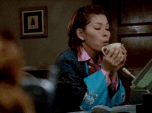 a woman in a blue robe drinks from a white cup