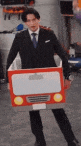 a man in a suit and tie is holding a cardboard box in the shape of a car .